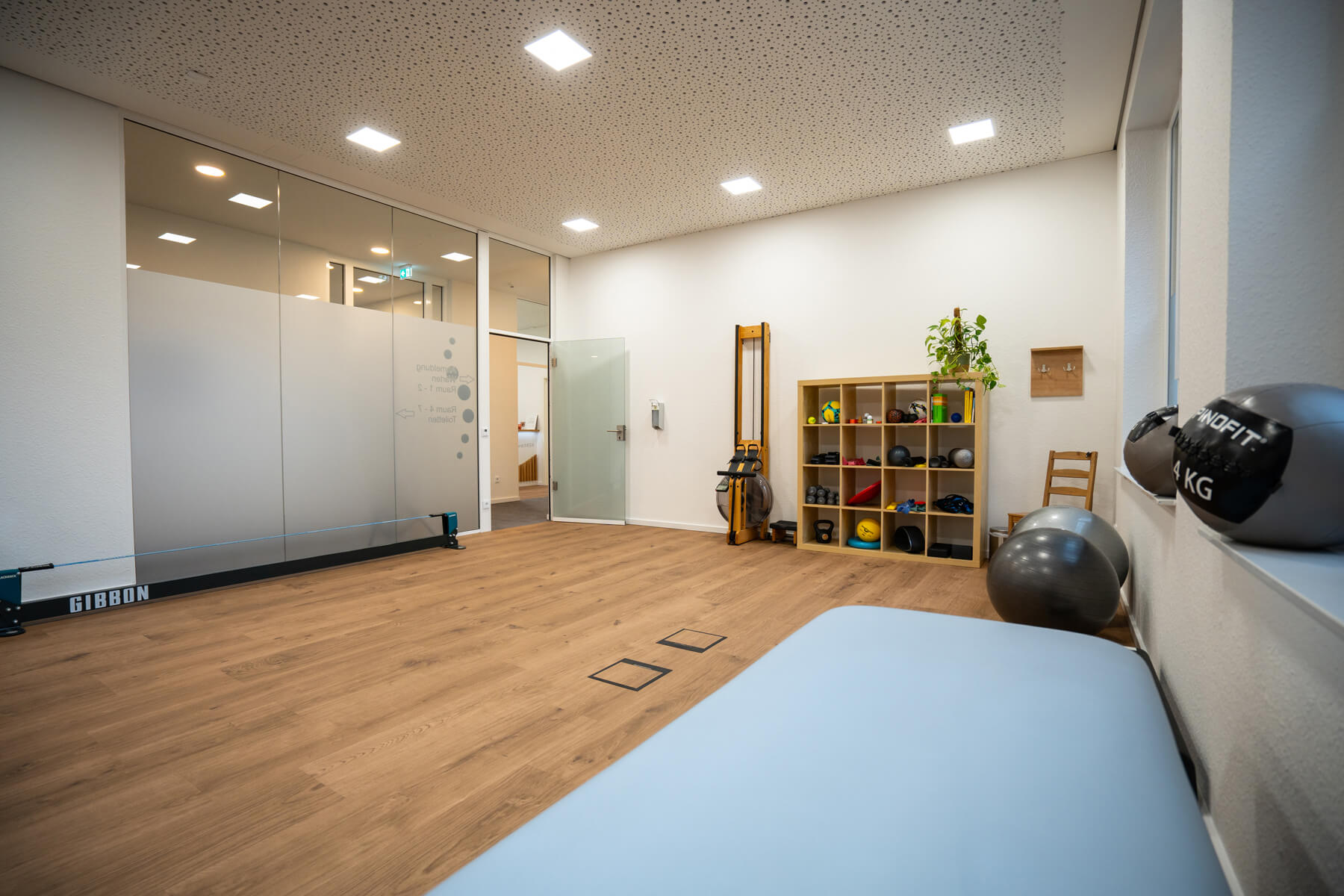 Ein moderner, heller Therapieraum mit Holzboden und einigen Geräten für die Therapie.